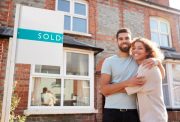 happy-couple-hugging-in-front-of-home-sold-sign