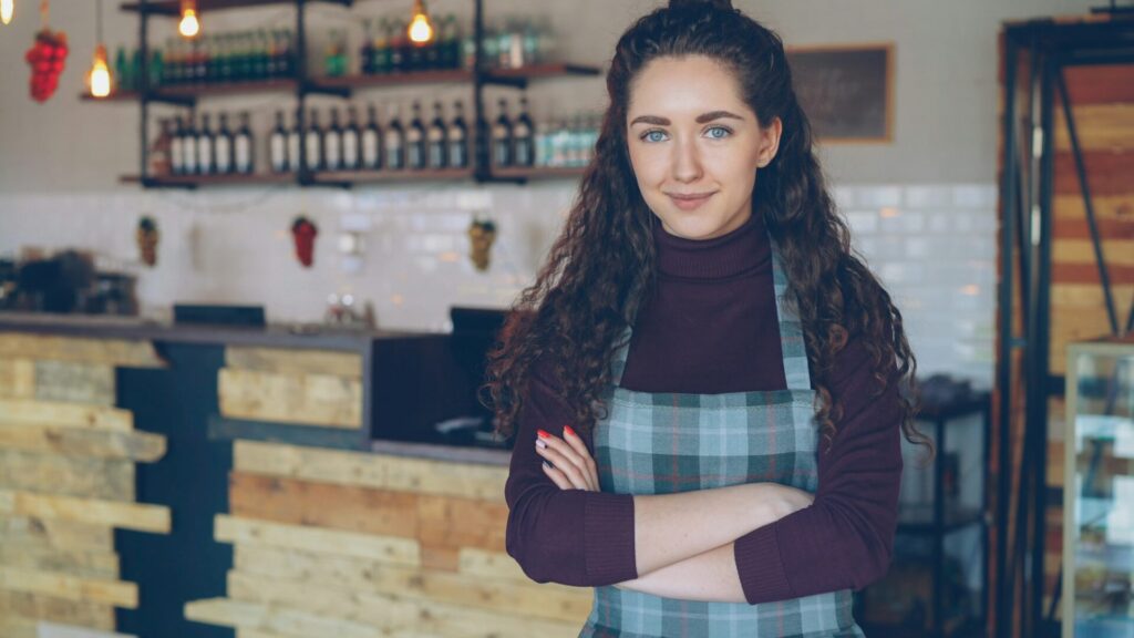 A smiling woman with her arms crossed stands in her coffee shop