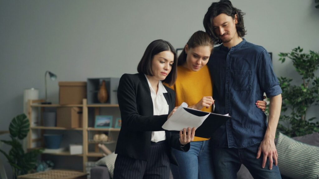 Real estate agent and a couple review a document together in a living room