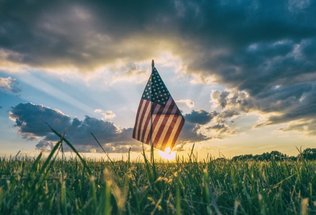 An American flag in a grass field under a sunset sky