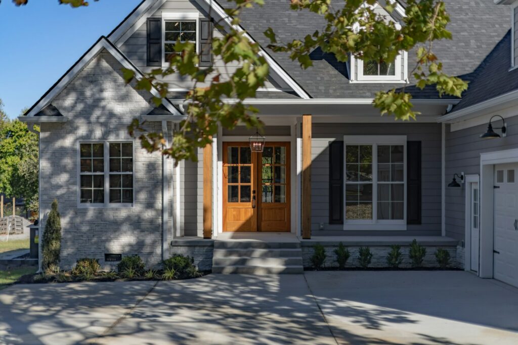 A gray suburban house with a stone base and wooden double doors