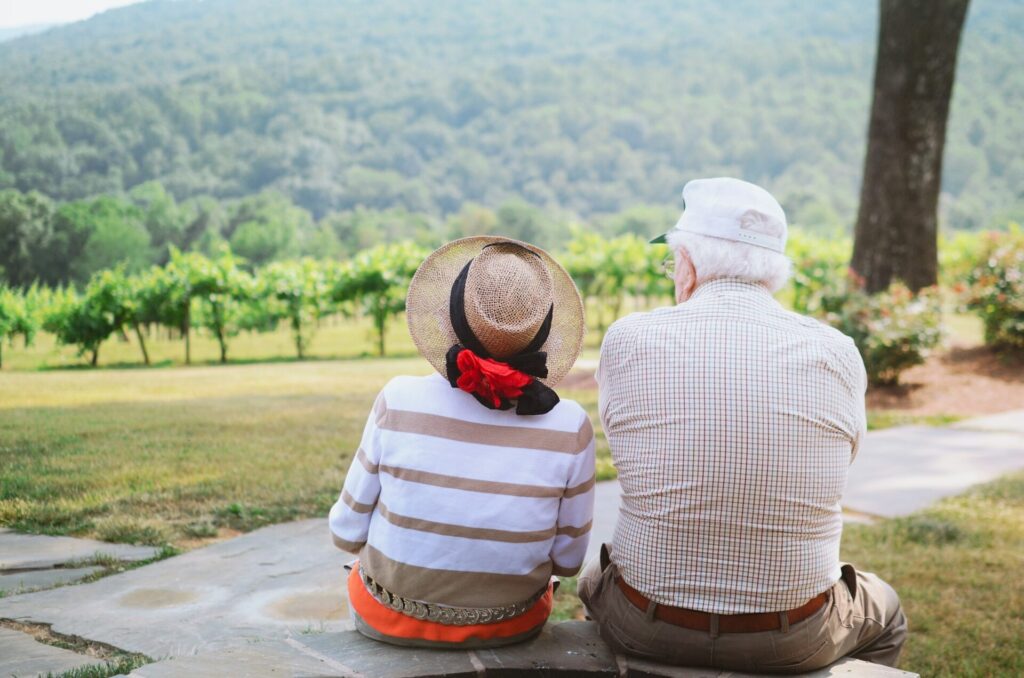 An older couple sits side by side and looks out over a vineyard