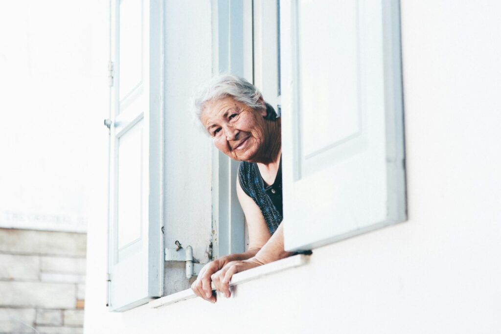 A smiling older woman leans out of an open window