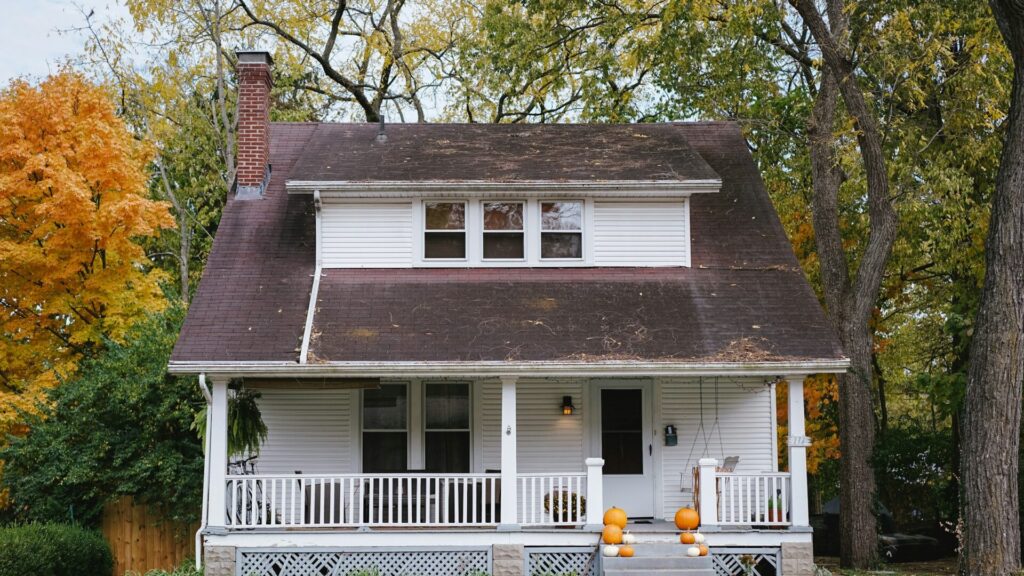Modest white house with a covered front porch among autumn trees