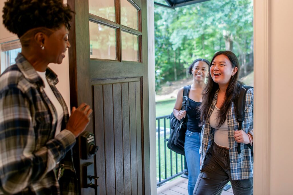 A woman opens her front door to two smiling visitors